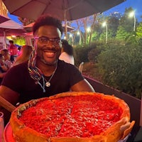 a man smiles while holding a large pizza